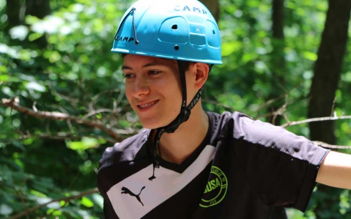 A person wearing a helmet smiles amongst a wooded area. 